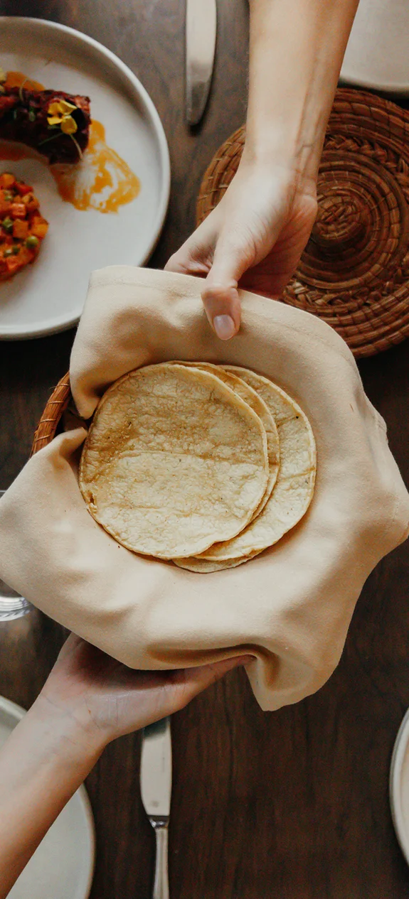 Two people passing a bowl of tortillas over a table