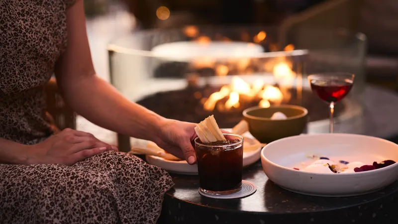 a person holding a drink sitting outside by a fire pit