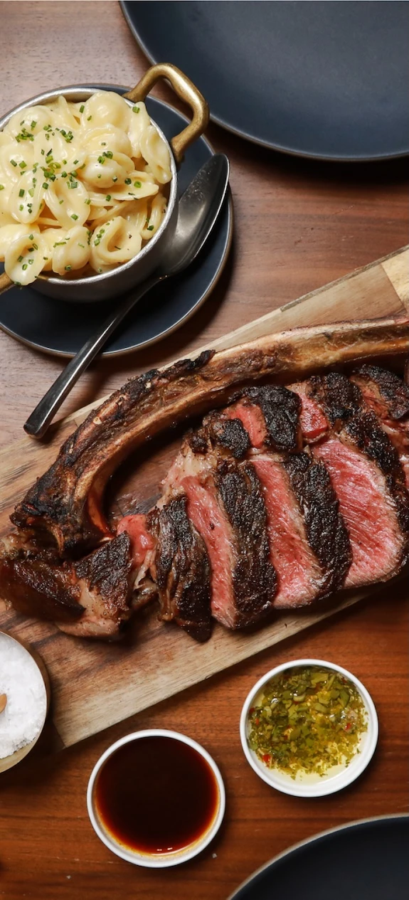 a cut up steak on a cutting board next to a bowl of mac and cheese