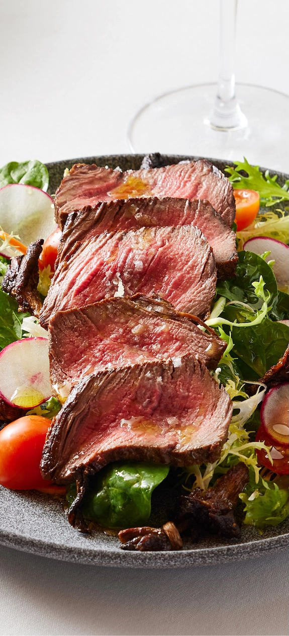 a cut up steak on a salad of fresh vegetables
